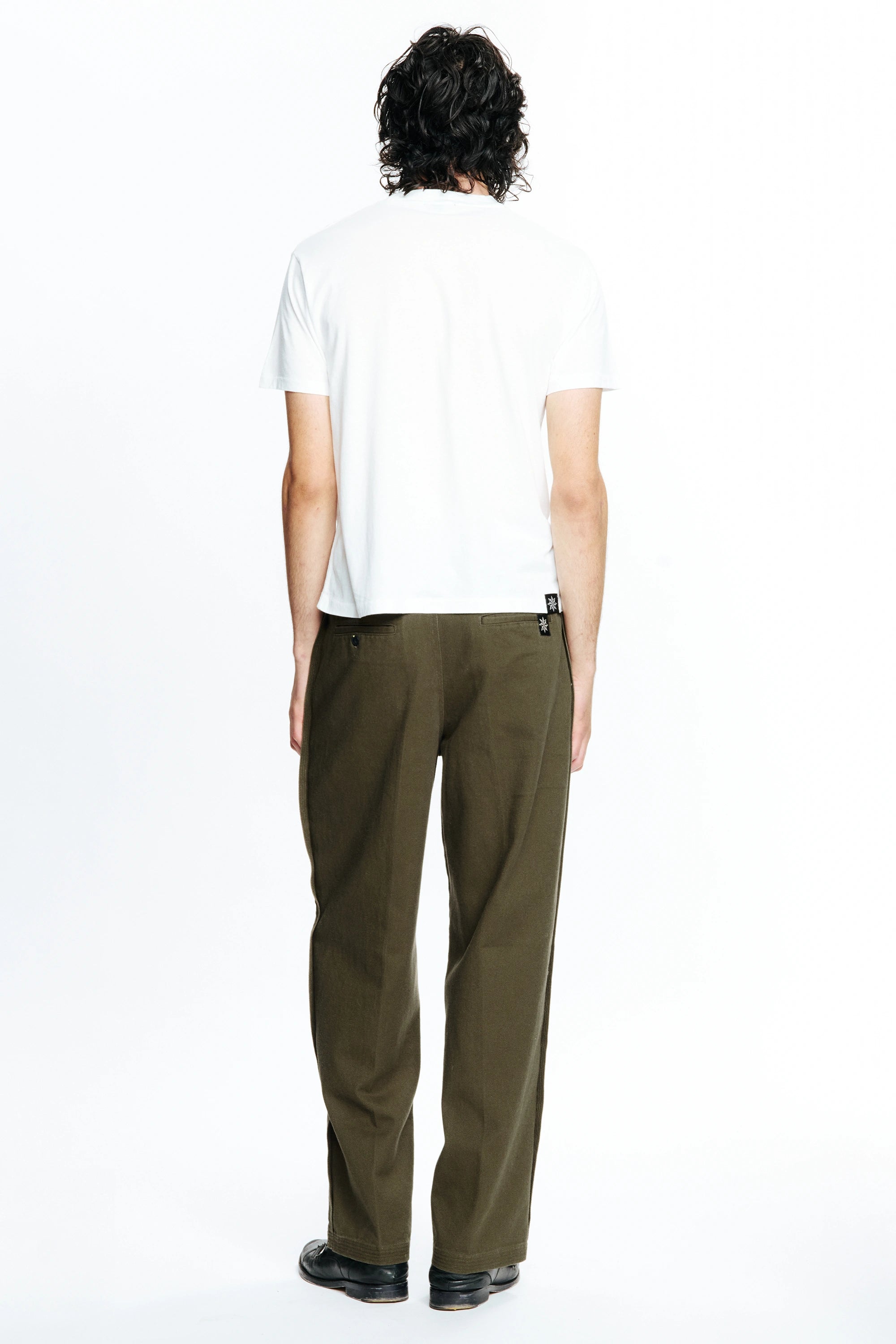 Person with their back turned wearing a white t-shirt and olive green pants on a white background