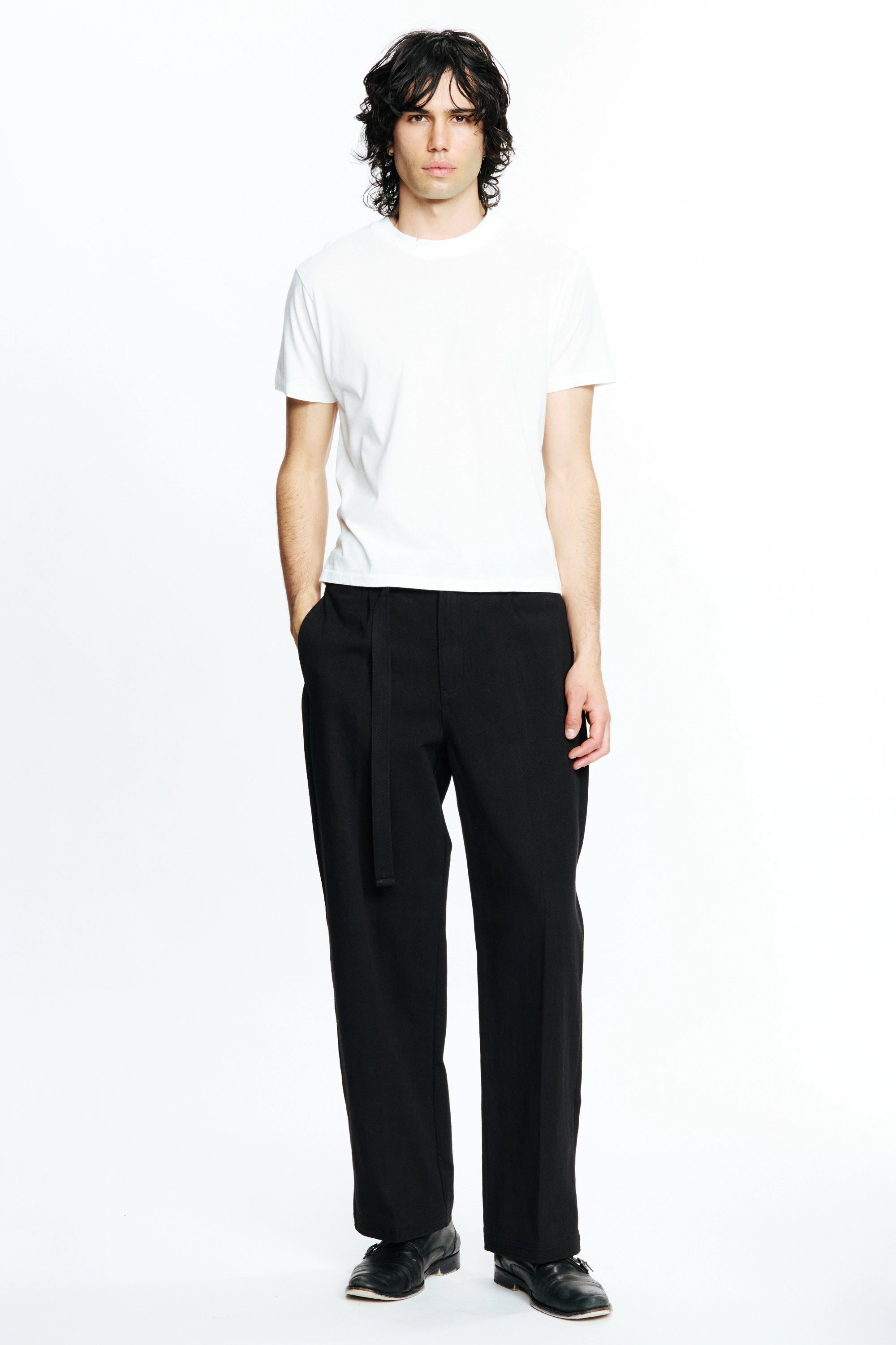 Person wearing a white t-shirt and black  pleated work pants on a white background